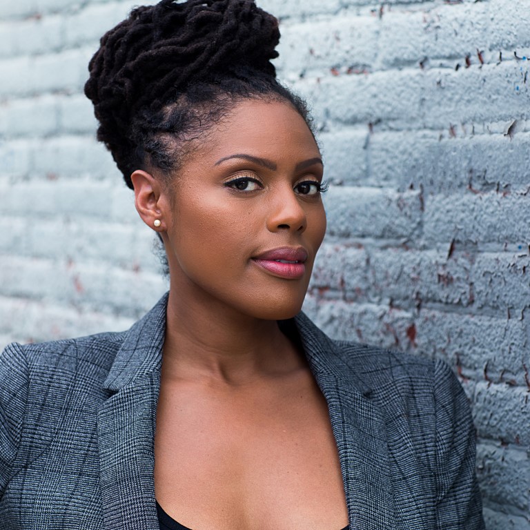 Black women with locked hair in a bun on her head with blue jacket on