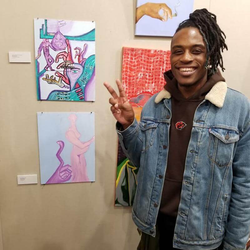 A student standing by his paintings.