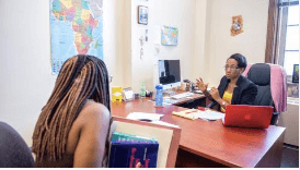 Female student sitting in front of desk speaking with female administrator